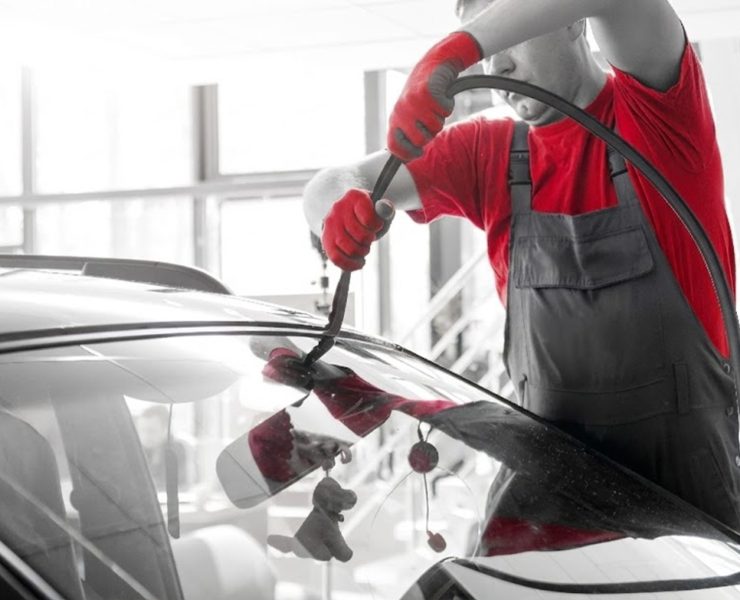 Automobile special workers remove old windscreen or windshield of a car in auto service station garage. Background
